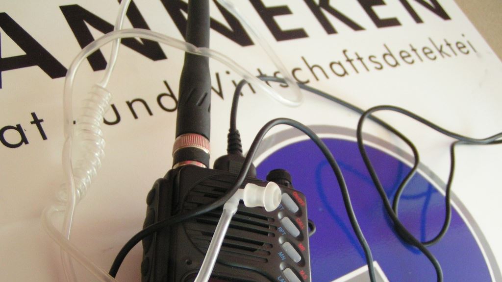 Ein Funkgerät der Marke Motorola mit angeschlossenem Kabel und einem geladenen Akku liegt auf einer Unterlage mit Textresten.