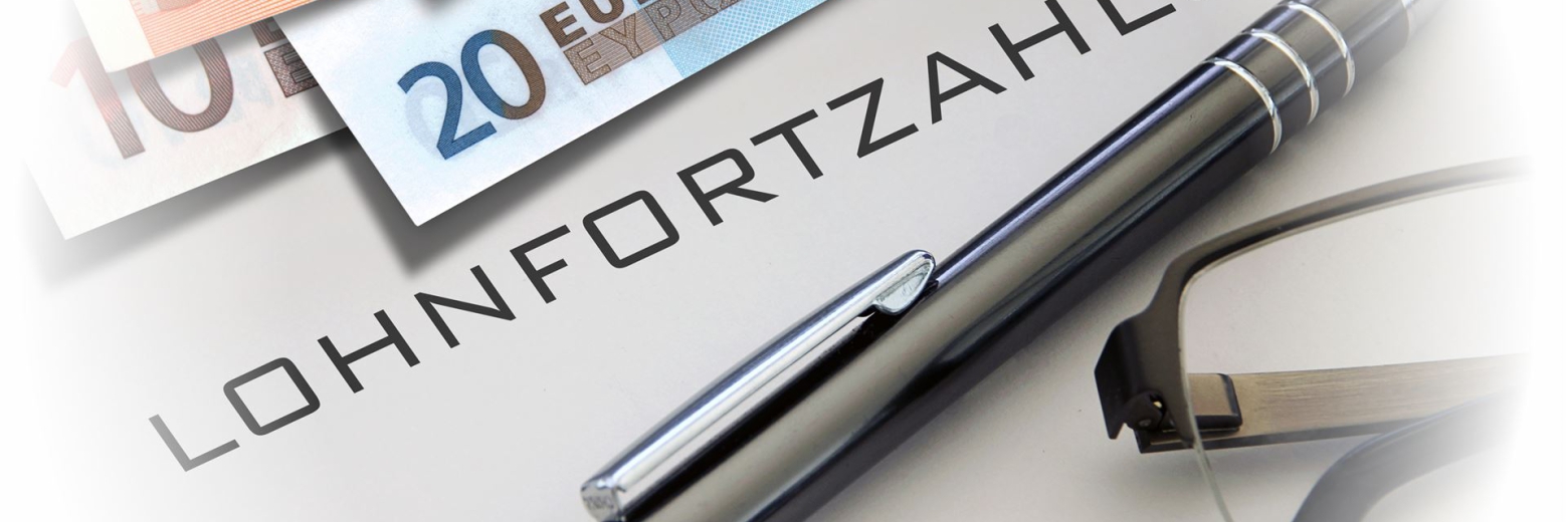 Mehrere Euro-Geldscheine, ein Kugelschreiber und eine Brille sind auf einer weißen Oberfläche angeordnet, mit dem Schriftzug LOHNFORTZAHLUNG.